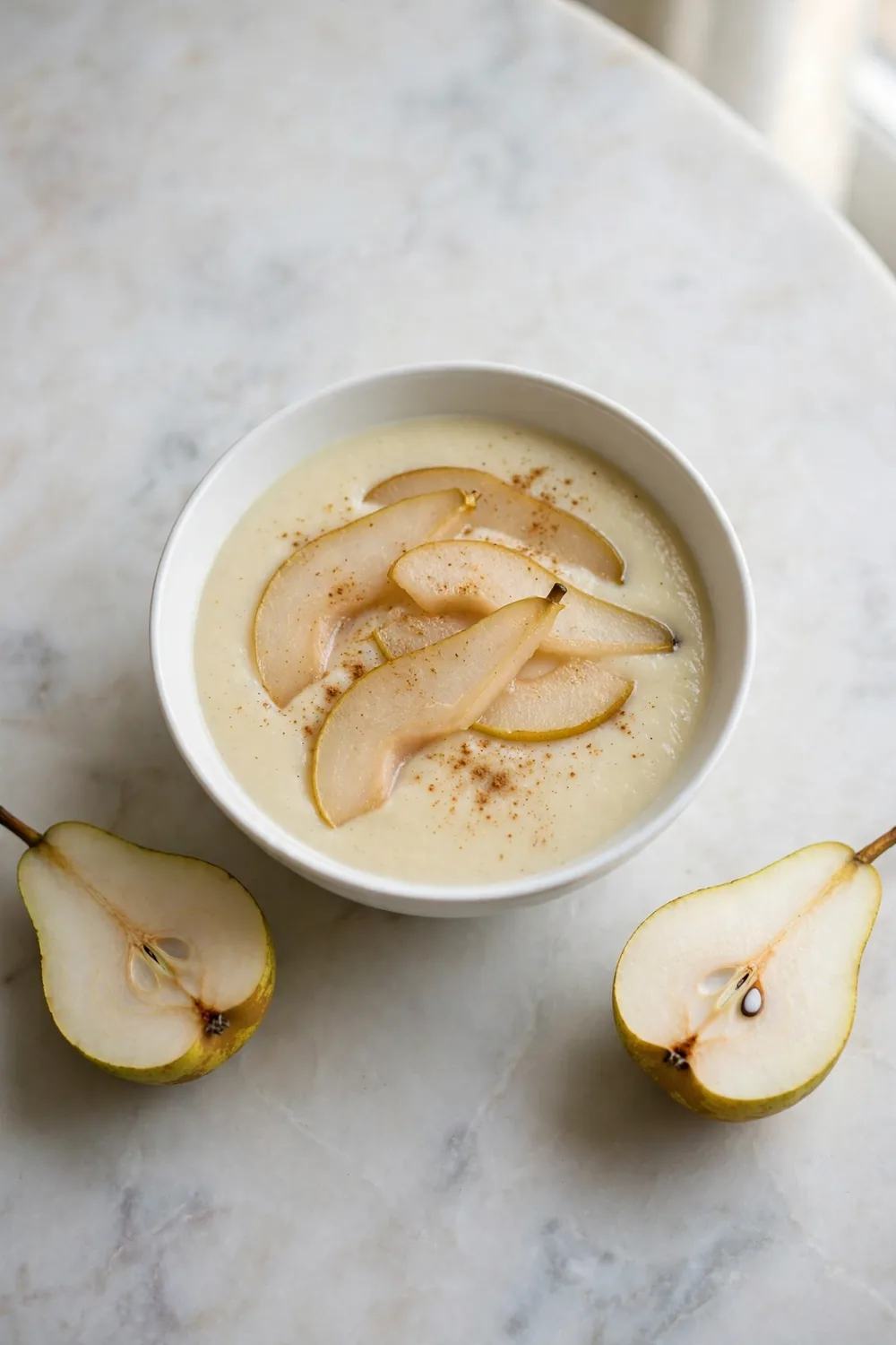 Parsnip soup with poached pear slices and warm spice in a white bowl