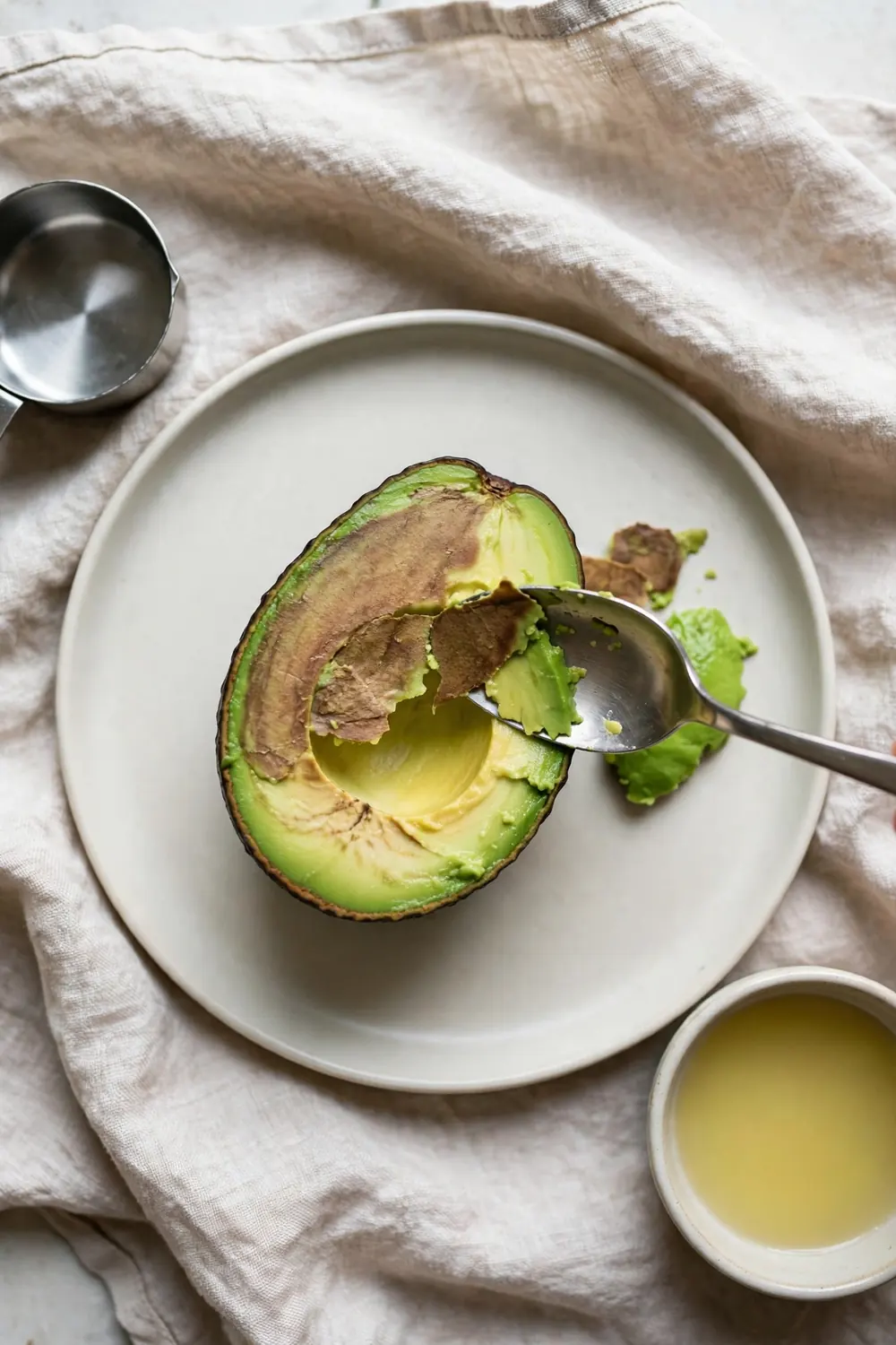 Spoon scraping a brown layer off a halved avocado
A thin brown layer can be scraped away, and the flesh under it stays fresh. Use a spoon to lift the brown layer off, and the green flesh shows again. Scraping works fast, and the avocado looks fresh once more.