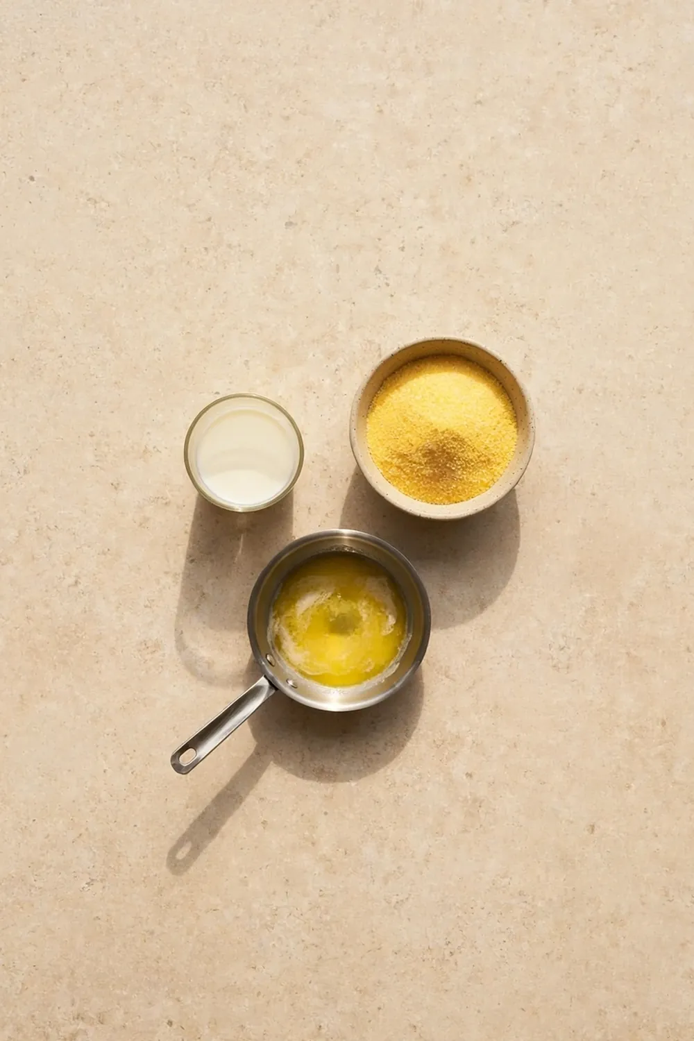 Melted butter in a bowl beside cornmeal and eggs on a counter