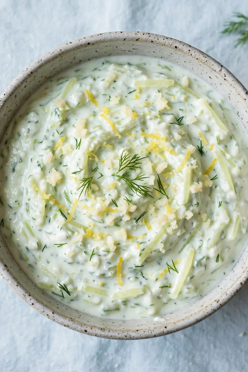Bright tzatziki dip with lemon slices and garlic in a ceramic bowl