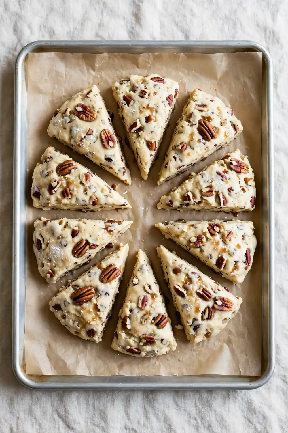 Unbaked maple pecan scone dough wedges with pecans on a tray