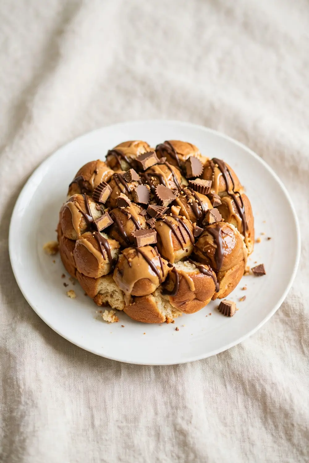 Vertical 2:3 portrait food photograph of peanut butter cup monkey bread on a white plate, golden pull-apart dough balls with peanut butter, chocolate drizzle and chopped peanut butter cups, the plate centered occupying the center 60 percent of the frame with balanced empty space around it, realistic serving and plate proportions, single focal point, warm natural light, photorealistic, no text