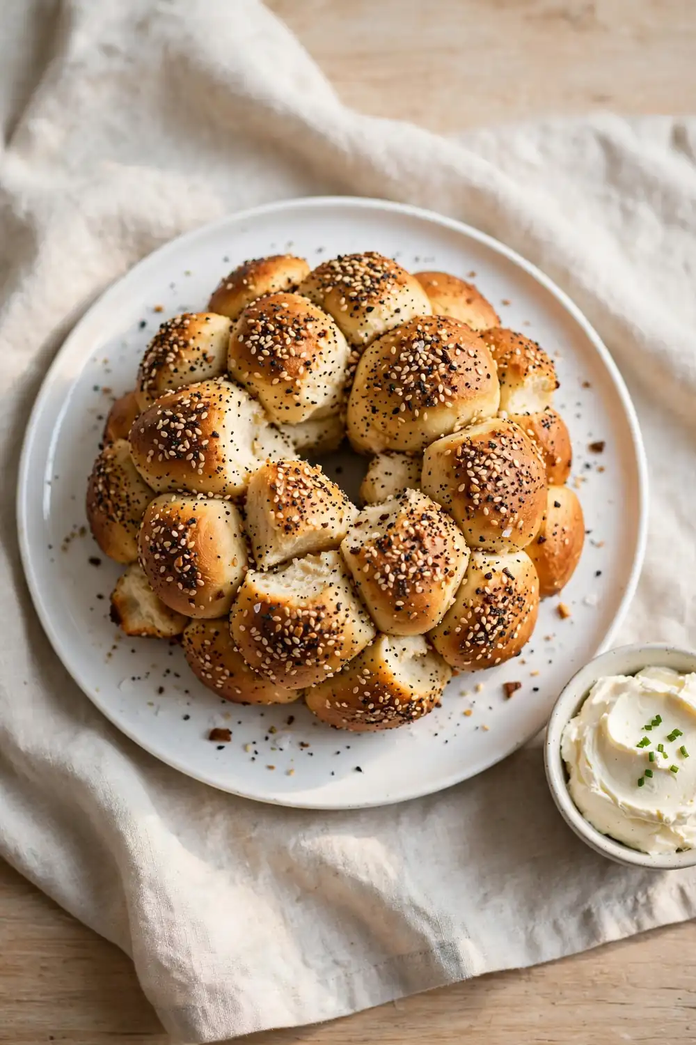 Vertical 2:3 portrait food photograph of everything bagel monkey bread on a white plate, golden pull-apart dough balls coated in everything bagel seasoning with sesame seeds, small bowl of cream cheese beside it, the plate centered occupying the center 60 percent of the frame with balanced empty space around it, realistic serving and plate proportions, single focal point, warm natural light, photorealistic, no text