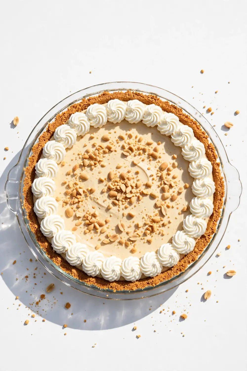 No-bake peanut butter dessert in a glass dish with piped cream and crushed peanuts