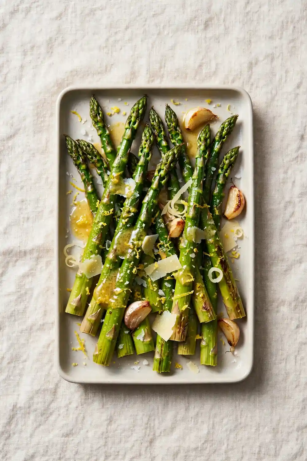 Roasted asparagus drizzled with garlic butter and lemon zest on a tray