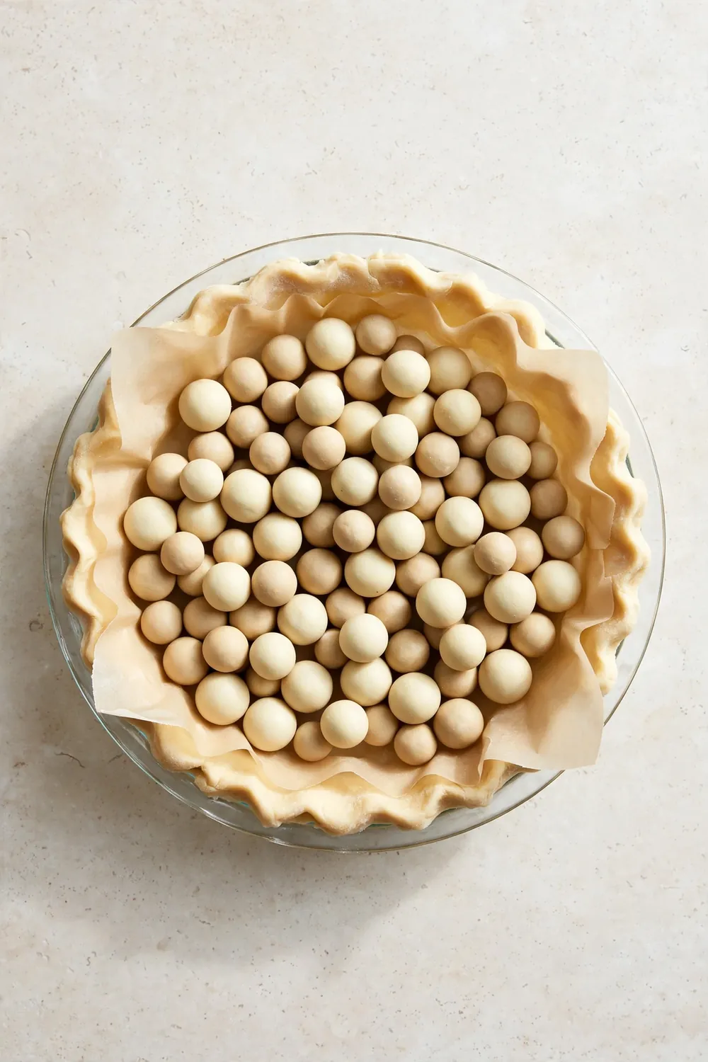 Empty quiche crust lined with parchment and pie weights ready for blind baking