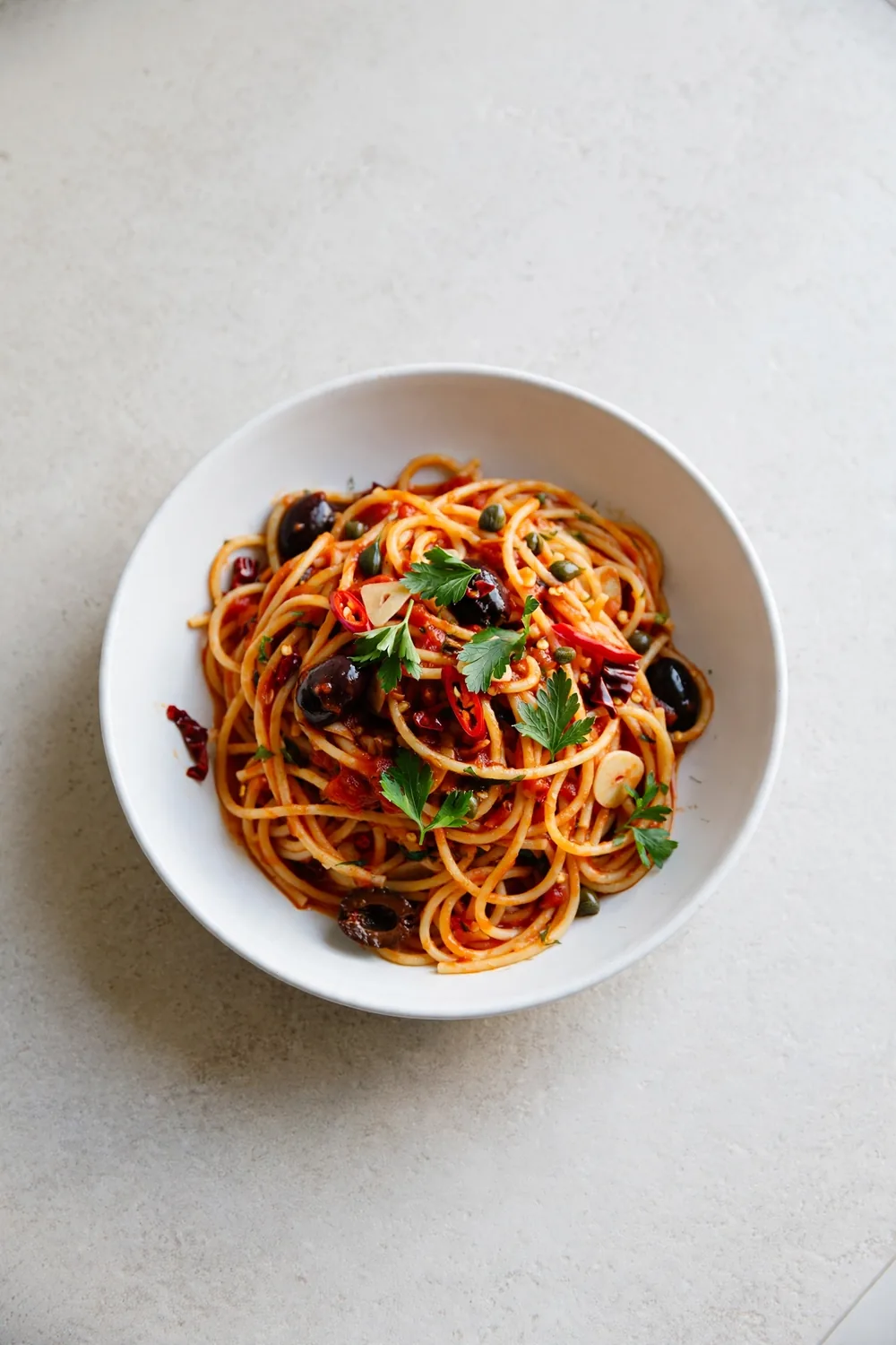 Spaghetti in tomato sauce with olives, capers, chili, and parsley