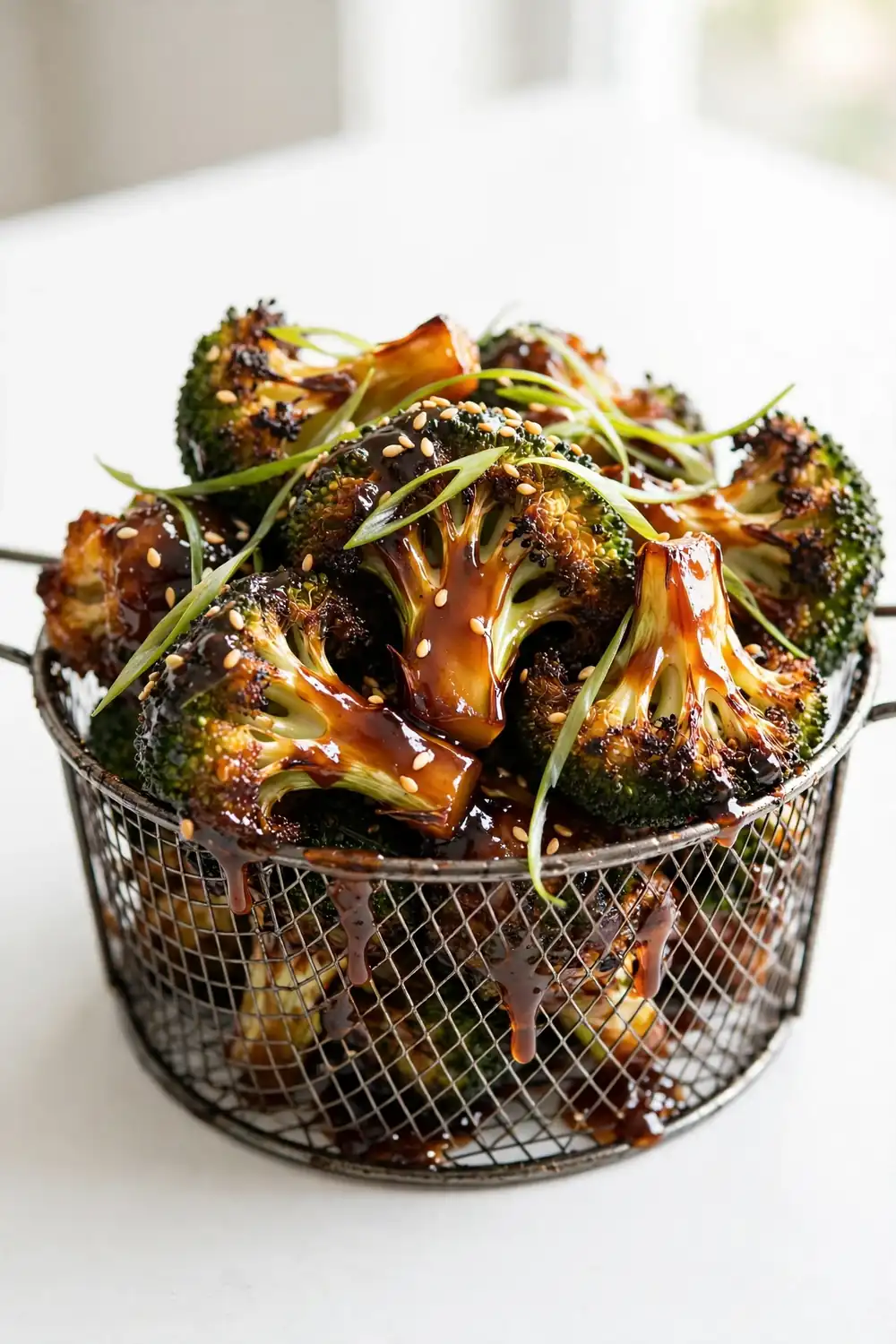 Crispy air fryer broccoli florets with caramelized edges in a metal basket with sesame seeds