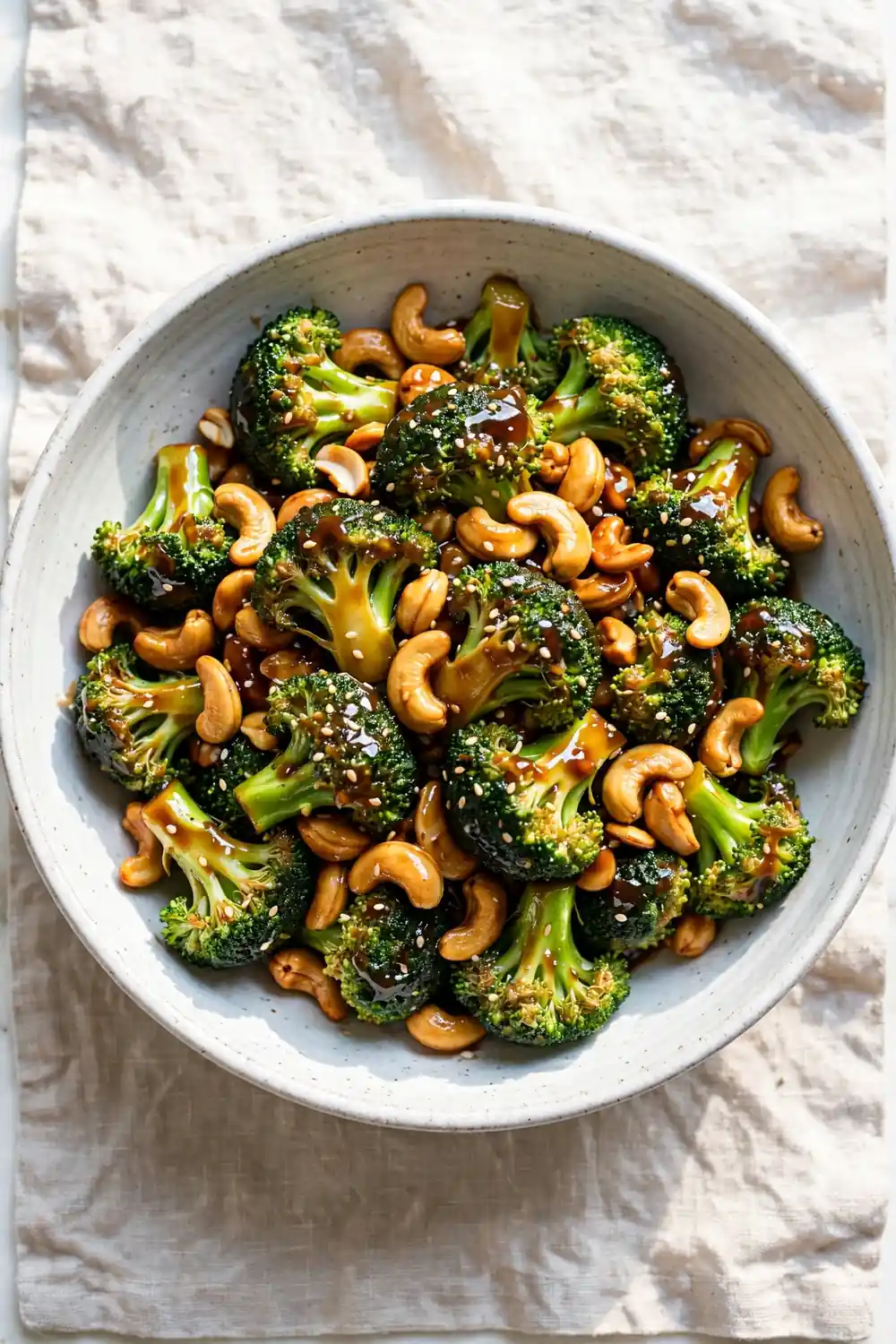 Broccoli florets tossed with roasted cashews and sesame seeds in a wide serving bowl