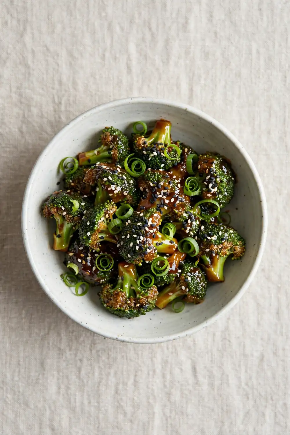 Broccoli florets with black and white sesame seeds and scallion curls in a ceramic bowl