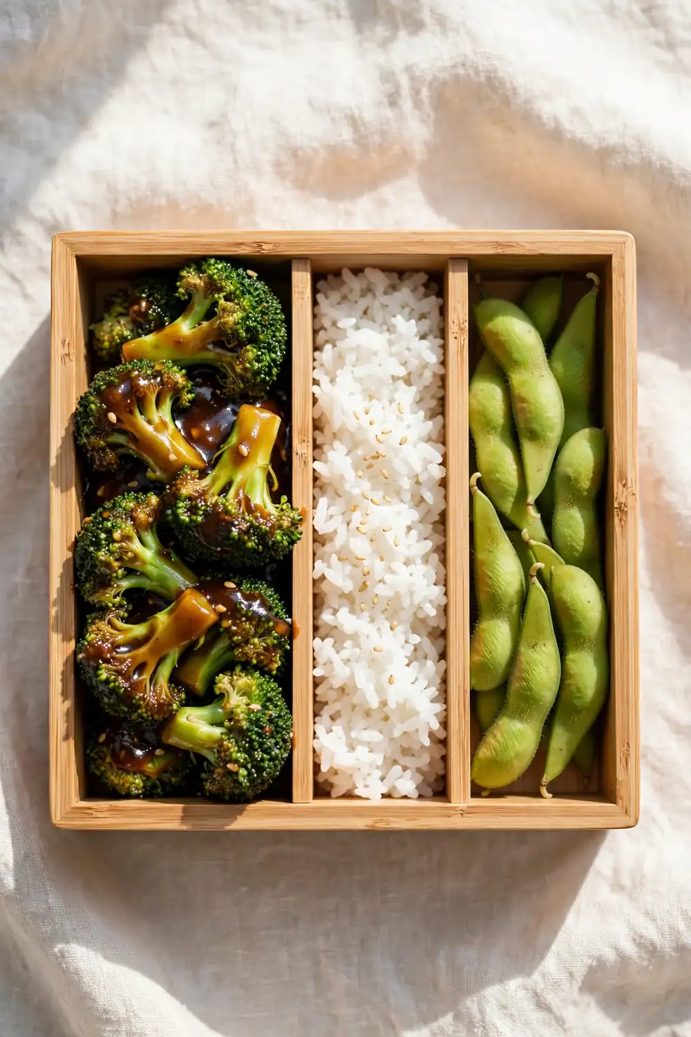 Broccoli florets packed in a compartment lunch box beside rice and edamame